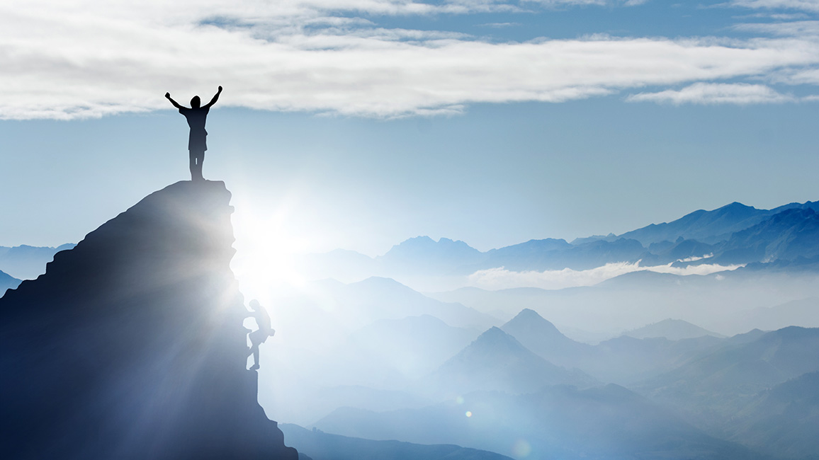 Mensch steht auf Bergspitze und reißt die Arme nach oben; © Adobe Stock / Visions-AD