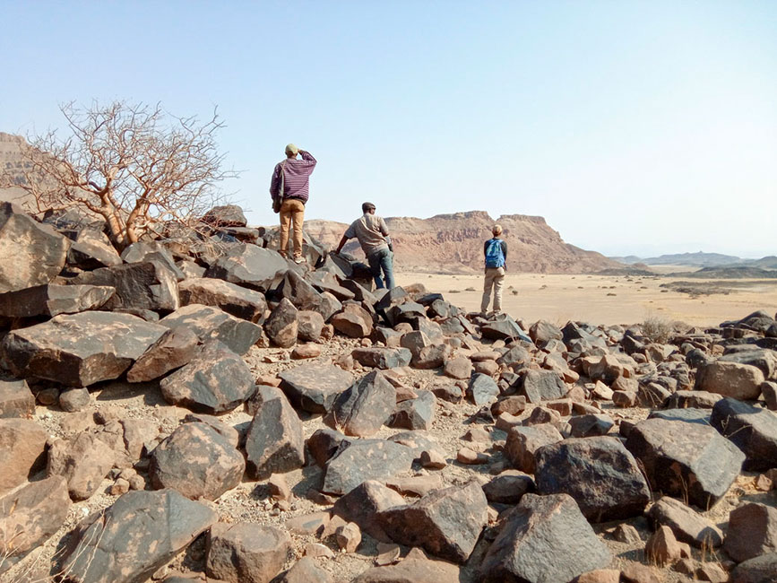 drei Männer stehen auf einem Hügel aus Steinen in einer Wüstenlandschaft
