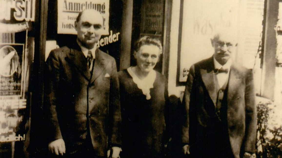 Kurt, Leonore und Hugo Friedlaender (v. l. n. r.) vor ihrem Lebensmittelgeschäft in Berlin Pankow, ca. 1936, Fotografie, 13 x 8,6 cm, unbekannte:r Fotograf:in. 