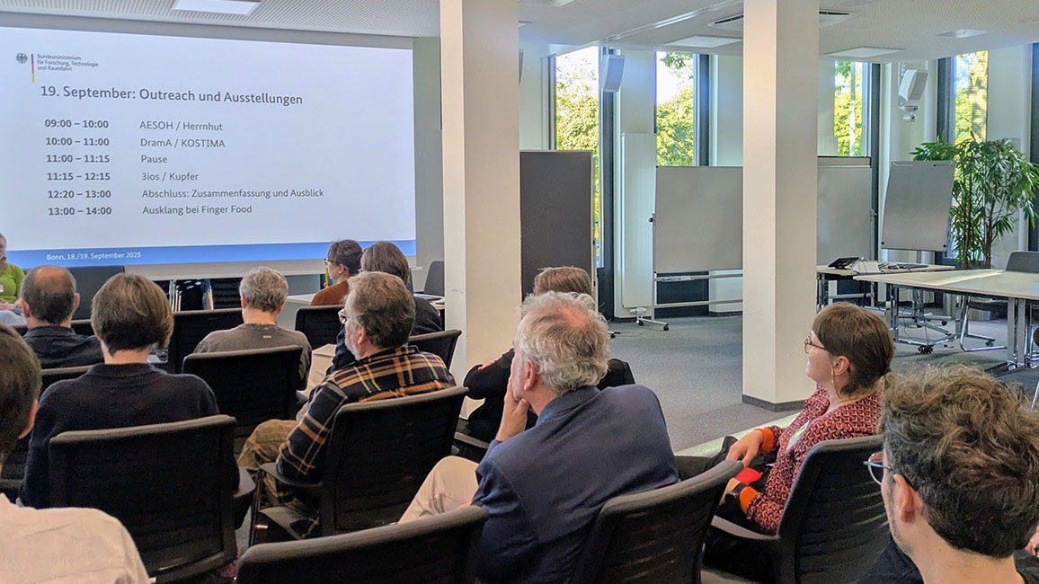 Personen sitzen bei einer Veranstaltung auf Stühlen und schauen nach vorne zur Präsentation