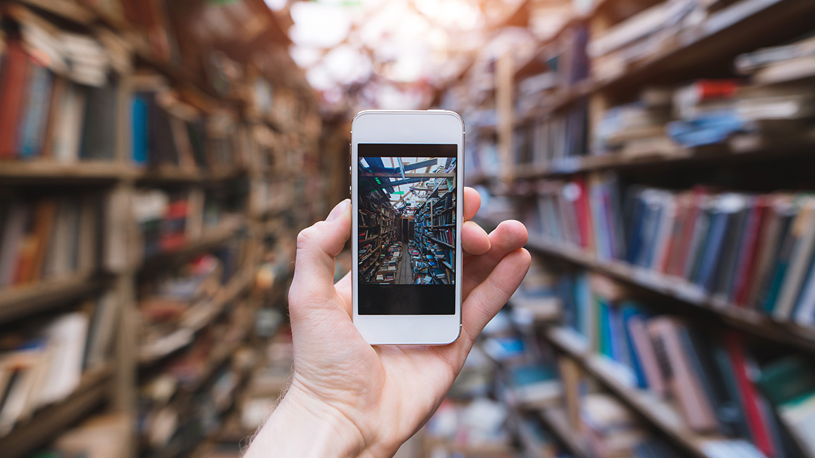 Jemand fotografiert mit Smartphone eine Bibliothek; Adobe Stock/bodnarphoto 